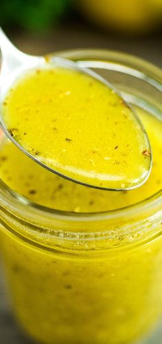 a spoon full of yellow liquid sitting on top of a glass jar filled with something