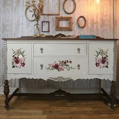 a white dresser with flowers painted on the front and drawers, along with two framed pictures