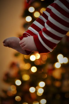 a child's hand holding an object in front of a christmas tree with lights