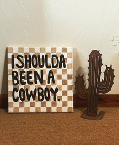 a sign that says i should be a cowboy next to a cactus and a wooden stand