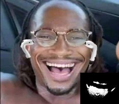 a man with glasses and headphones in his ears smiles at the camera while sitting in a car