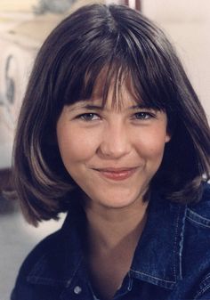 a close up of a person wearing a denim shirt and smiling at the camera with a smile on her face