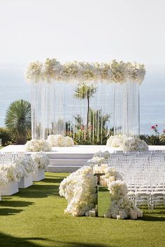 an outdoor ceremony setup with white flowers and greenery on the grass, overlooking the ocean