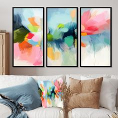 three abstract paintings hang on the wall above a white couch in a living room with pillows