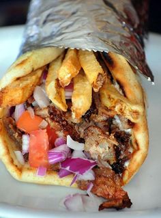 a wrap filled with meat and vegetables on top of a white plate