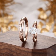 two gold wedding rings sitting on top of a wooden box next to another ring with a heart shaped diamond in the middle