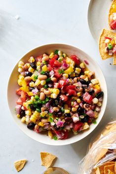 a white bowl filled with corn salad next to tortilla chips on a table