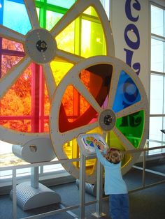 a young boy standing in front of a colorful wheel on display at an art museum