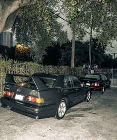 two cars parked next to each other in front of a fenced area with trees