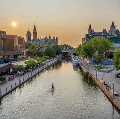 a person riding a paddle board on a river in the middle of a city at sunset