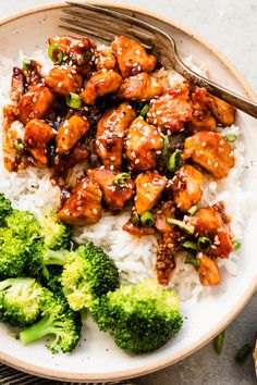 a white plate topped with rice and broccoli covered in chicken sauce next to a fork