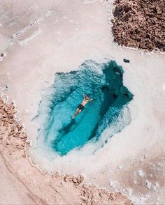 a person swimming in the water near some rocks and sand on the beach at low tide