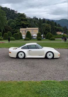 a white sports car parked in the middle of a parking lot next to some trees