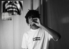 a man with dreadlocks standing in front of a curtain holding his hand up to his face