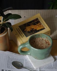 a cup of coffee sitting on top of a table next to a book and a plant