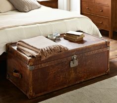 an old trunk sits on the floor in front of a bed with pillows and blankets