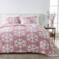 a pink and white comforter set with snowflakes on the bed in front of a window