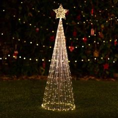 a lighted christmas tree in the grass at night with lights all around it and stars on top