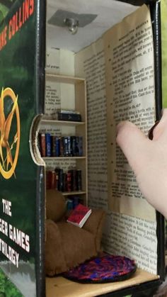 a hand is pointing at an open book in the shape of a doll's house