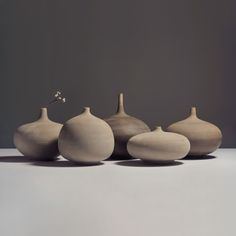 five white vases sitting on top of a table next to each other in front of a gray wall