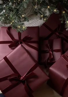 several wrapped presents under a christmas tree with lights on it's branches and red bows