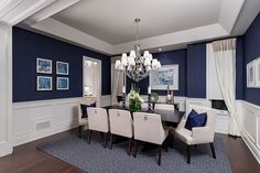 an elegant dining room with blue walls and white chairs, chandelier and pictures on the wall