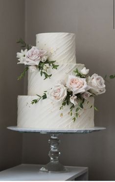 two tiered white wedding cake with pink roses and greenery on the top layer