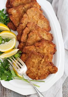 some fried food on a white plate with lemons and parsley