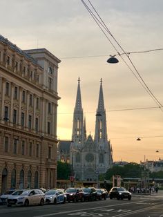 cars are parked on the side of the road in front of an old building with spires