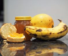 a banana, honey and orange peel on a table with some other fruit in the background