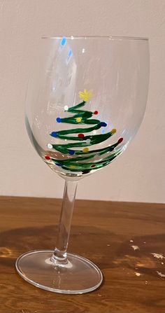 a wine glass with a christmas tree painted on the side and colored dots in the bottom