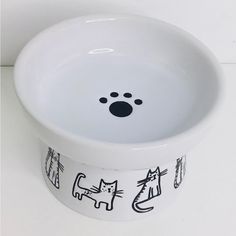 a white bowl with black cats and dogs painted on the side is sitting on a table