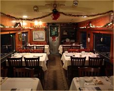 a dining car is decorated for christmas with lights on the ceiling and white tablecloths