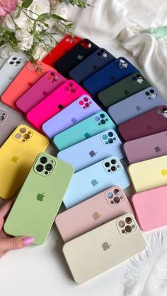 several colors of iphone cases sitting on top of a white table next to some flowers