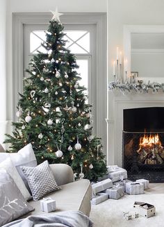 a decorated christmas tree in front of a fireplace with white and silver ornaments on it