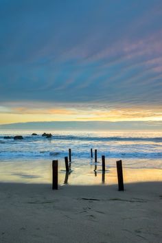 the beach is covered in water and wooden posts are sticking out of the sand as the sun sets