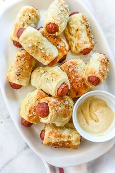 a white plate topped with pigs in a blanket and some dipping sauce