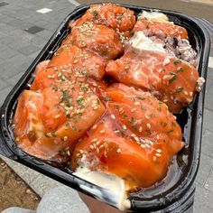 someone holding up a tray of food with meat and vegetables in it on the street