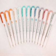 six different colored pens lined up next to each other on a white surface with writing