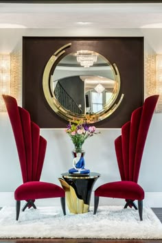 a room with two red chairs and a round mirror on the wall above it is an area rug