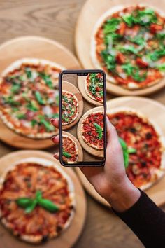 a person taking a photo of pizzas on their cell phone with the other hand