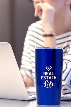 a woman sitting in front of a laptop computer with a blue coffee mug on her lap