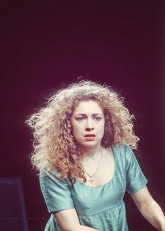 a woman with long curly hair is holding a tennis racquet