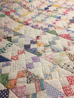 an old quilt is laying on top of a bed with white sheets and colorful patterns