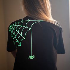 a woman wearing a black shirt with green spider web on it's chest and back