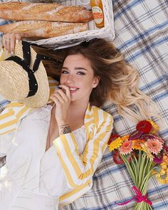 a woman laying on top of a bed next to flowers and bread in a basket