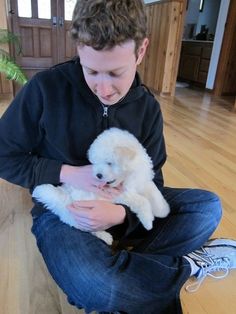 a boy sitting on the floor holding a white dog in his lap and looking down