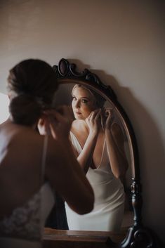 a woman in a white dress is looking at her reflection in the mirror while brushing her teeth