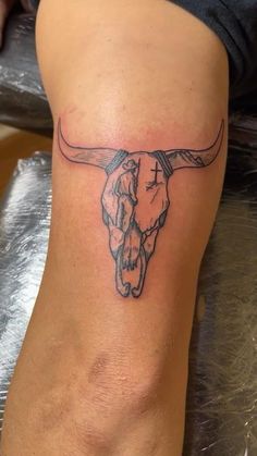 a tattoo on the leg of a woman with a bull's head and cross