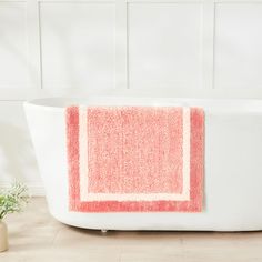 a bathtub with a red and white towel on it next to a potted plant